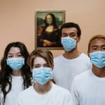 A diverse group wearing masks stands in front of a masked Mona Lisa painting.
