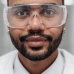 Close-up portrait of a male scientist wearing safety goggles in a lab.